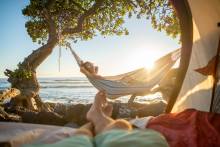 couple on beach one in hammock, one lounging on chair